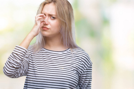 年轻的金发女人在孤立的背景上闻到了一些臭味和恶心，难以忍受的气味，用手指在鼻子上屏住呼吸。坏气味的概念。