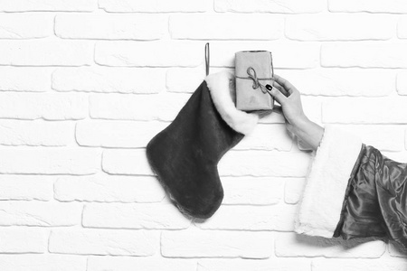 女性手得到礼物包裹在工艺纸从圣诞长袜或圣诞树靴子在白色砖墙背景