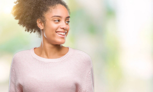 年轻的非洲美国女人穿着冬天的毛衣，在孤立的背景上看着一边，脸上带着微笑，自然的表情。 自信地笑着。