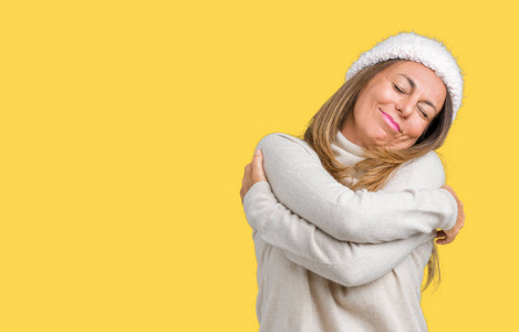 美丽的中年妇女穿着冬天的毛衣和帽子,在孤立的背景下拥抱自己,快乐而