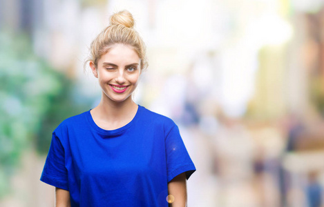 年轻漂亮的金发碧眼的女人穿着蓝色的T恤，在孤立的背景上眨眼，看着镜头，的表情，开朗和快乐的脸。