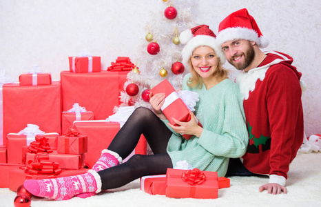 情侣在爱享受圣诞节节日庆祝。一起庆祝圣诞节爱的夫妇抱着微笑, 而打开礼物与圣诞树的背景。家庭圣诞节传统