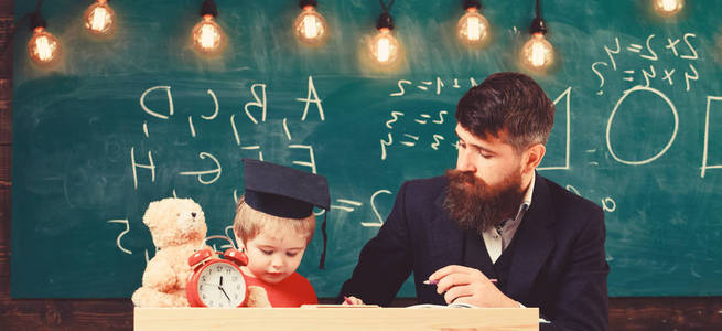 父亲教儿子数学。热心的孩子和老师一起学习。数学课的概念。教师在正式穿戴和学生在 mortarboard 在教室, 黑板在背景上