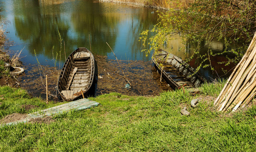 古老的木制蓝色划艇渔船在一个美丽的春天阳光明媚的一天在杂草丛生的湖航道。 在湖岸的芦苇中划渔船是中巷的典型景观