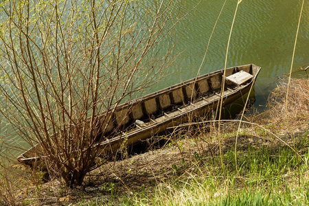 古老的木制蓝色划艇渔船在一个美丽的春天阳光明媚的一天在杂草丛生的湖航道。 在湖岸的芦苇中划渔船是中巷的典型景观