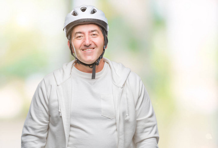 英俊的资深骑自行车的男子戴着自行车头盔，偏僻，脸上挂着快乐的表情，微笑着露出自信的牙齿