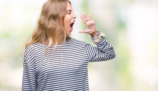 美丽的年轻金发女人穿着条纹毛衣，在孤立的背景上大声喊叫和尖叫，手在嘴上。 交流概念。