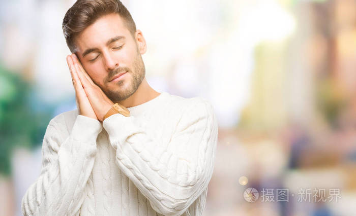 年轻的帅哥穿着冬天的毛衣,在与世隔绝的背景下睡觉,疲倦的做梦,双手