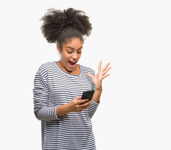 年轻的美国妇女使用智能手机在孤立的背景下发短信，非常高兴和兴奋的胜利者表情庆祝胜利，微笑着尖叫，举起手