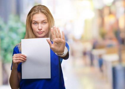年轻的白种人妇女拿着空白纸在孤立的背景上，张开手做停止标志，严肃而自信的表情防御手势