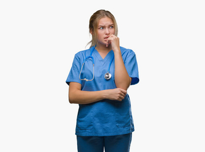 年轻的高加索医生女人穿着外科医生制服，在孤立的背景上看起来压力和紧张，双手咬着嘴的指甲。 焦虑问题。
