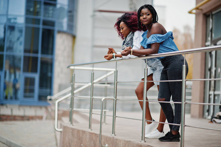 两位有吸引力的非裔美国妇女在现代多层建筑的栏杆附近摆好姿势。