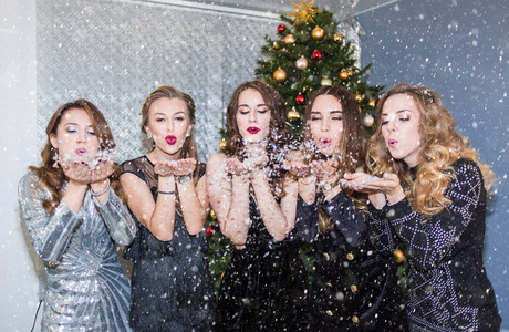 美丽的年轻女人在圣诞节聚会上玩得很开心，吹走了纸屑和雪送的吻。 新年节日庆祝晚会概念