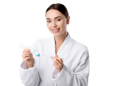 微笑的女人穿着白色浴袍，把牙膏和牙刷隔离在白色上
