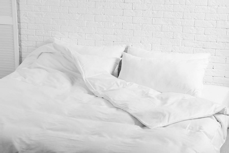 大舒适的床，枕头和毯子靠近白色砖墙在室内。 时尚内饰