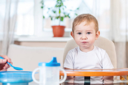 妈妈在厨房里用一勺粥喂宝宝伸出手..儿童在吃健康食物时的情绪。