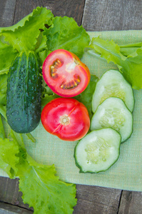 切片的黄瓜和西红柿躺在绿色的餐巾纸上，旁边是莴苣叶子，古老的深色木制背景，垂直拍摄。