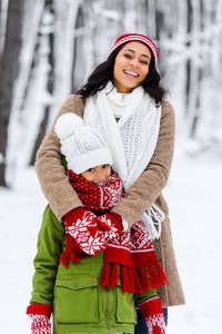 微笑着的非裔美国人母亲和女儿在冬季公园看相机