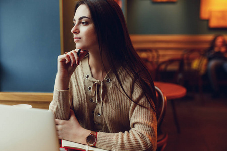 漂亮的黑发女人在咖啡馆工作，戴着眼镜，在窗户附近的笔记本电脑里聊天。 图像