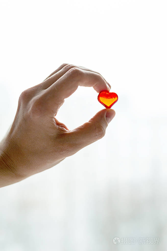 手指拿着一颗红色的小塑料心脏爱和心脏健康的象征