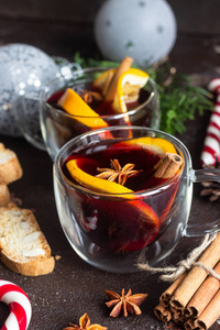 玻璃杯的热覆膜葡萄酒或Gluhwein与香料和橙色碎片在深棕色的背景。 圣诞覆盖葡萄酒。 寒假的传统饮料。 复制空间。