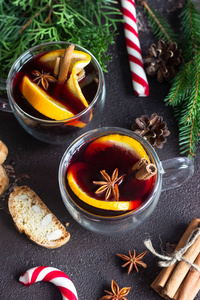 玻璃杯的热覆膜葡萄酒或Gluhwein与香料和橙色碎片在深棕色的背景。 圣诞覆盖葡萄酒。 寒假的传统饮料。 复制空间。
