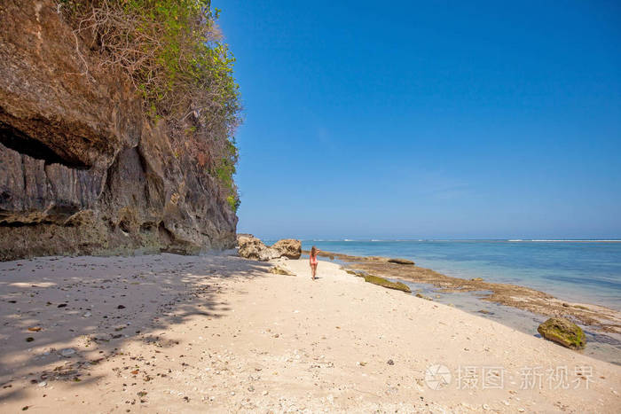 海滩上穿着粉色泳衣的年轻女子的背影