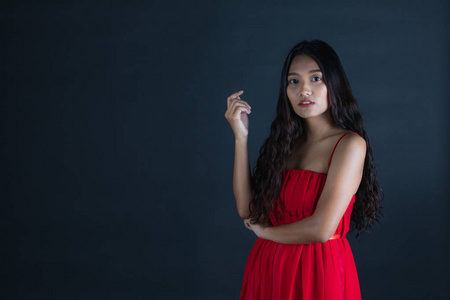 摄影棚肖像，年轻美丽的亚洲女人，穿着红色连衣裙，带着怀疑的脸，表情，在黑暗的背景上交叉地看着。