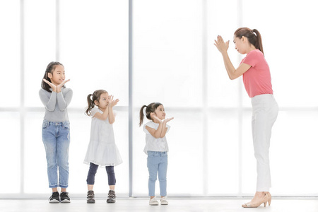 穿着粉红色衬衫的亚洲女人教孩子们玩他们站在大白窗前的东西。