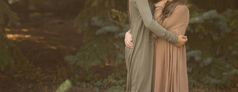 两个女孩拥抱在森林里的街道上。 友谊。 穿着绿色和棕色的连衣裙。 一个公园。 自动