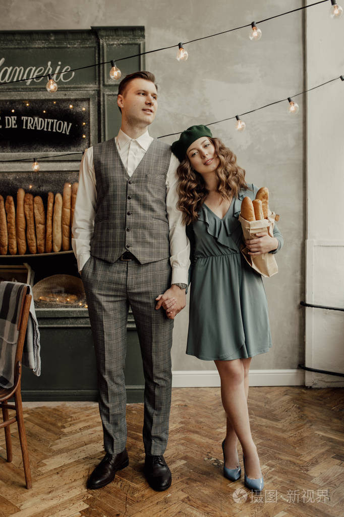 时尚的男人握着女孩的手.她戴着绿色贝雷帽, 拿着面包.腿在他们身后