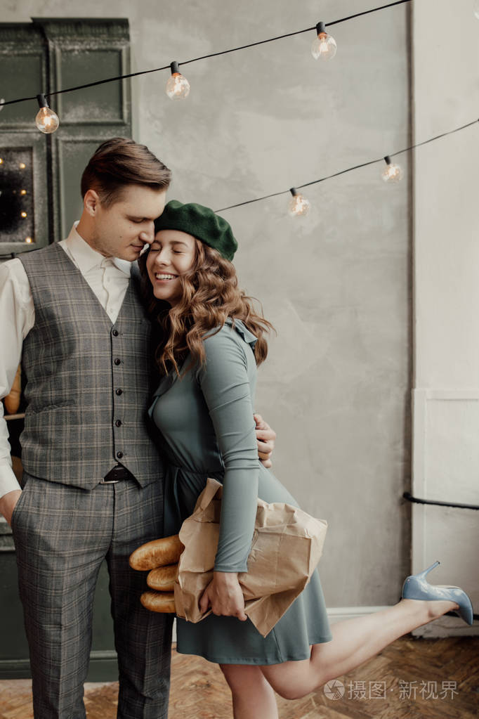 时尚的男人在亲吻她脸颊上的女孩.她戴着绿色贝雷帽, 拿着面包.