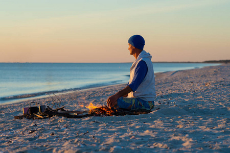 旅行者坐在海边的篝火旁沉思，欣赏海上的日落。 去海边旅行真棒。