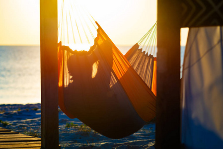 曼在废弃的平房阳台上的吊床上放松，在日落时欣赏绿松石海。 去海边旅行真棒。 后视背光。