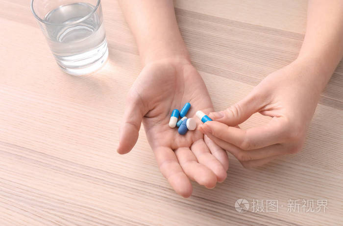 年轻女子在餐桌上吃药,注意力集中在手上照片-正版商用图片16dcyv-摄
