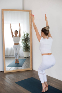 运动中的年轻女子在家里在镜子前做瑜伽