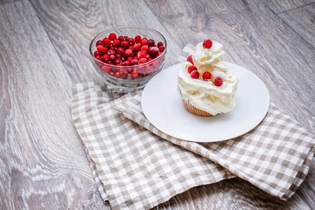 在一张轻盈的桌面上，在一张亚麻餐巾纸上，在一个茶托蛋糕上，加鲜奶油和新鲜浆果，一个有红色浆果的碗。 节日糕点的组成。