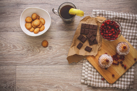 在亚麻餐巾纸餐巾纸上的一个轻木桌面上，有一个切割板，上面有两个松饼，一个破碎的巧克力棒和鲜红色的浆果，放在一棵小树上，旁边是一个