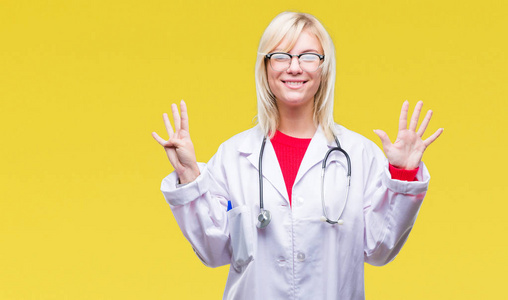 年轻漂亮的金发医生女人穿着医疗制服，在孤立的背景上显示和指着第九个手指，同时微笑自信和快乐。
