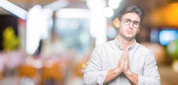 年轻的英俊男子戴着眼镜，在孤立的背景下乞讨和祈祷，双手一起祈祷，脸上充满希望的表情，非常情绪化和担忧。 请求原谅。 宗教观念。