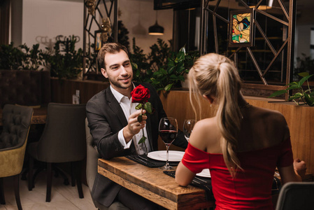 一个英俊的男朋友坐在餐馆里给女朋友送红玫瑰