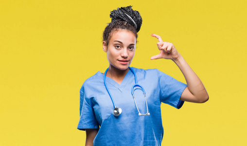 年轻的辫子非裔美国女孩专业外科医生在孤立的背景上微笑和自信的手势与手做大小标志与手指，同时看和相机。 测量概念。