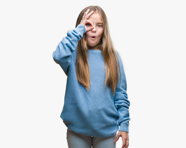 年轻漂亮的女孩穿着冬天的毛衣，在孤立的背景上做着OK的手势，惊讶的脸眼睛透过手指看着。 不相信的表情。