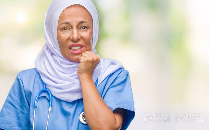 中年高级阿拉伯护士妇女戴着头巾，背景与世隔绝，看上去压力很大，紧张，双手咬着嘴的指甲。 焦虑问题。