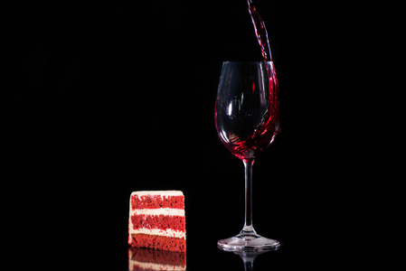 一块蛋糕，靠近一杯红酒，隔离在黑色上