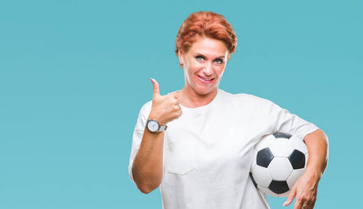 有魅力的高白种人红头发的女人拿着足球在孤立的背景下快乐，大大的微笑，做着好的，用手指签个字，很好的标志