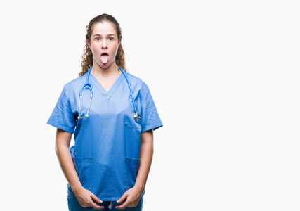 年轻的黑发医生女孩穿着护士或外科医生制服，在孤立的背景上伸出舌头，以有趣的表情高兴。 情感概念。