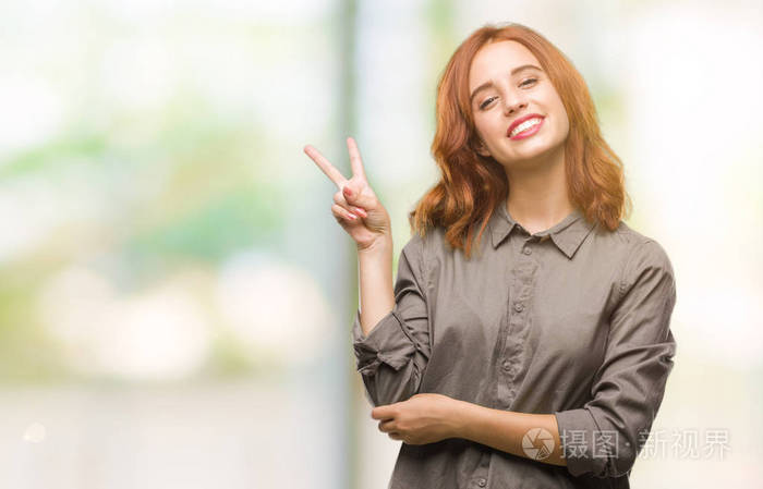 年轻漂亮的女人在孤立的背景上微笑，快乐的脸对镜头眨眼，做胜利标志。 二号。