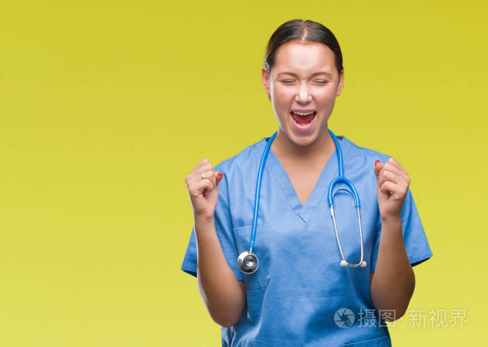年轻的白种人医生女士穿着医疗制服在孤立的背景下兴奋地成功举起双臂