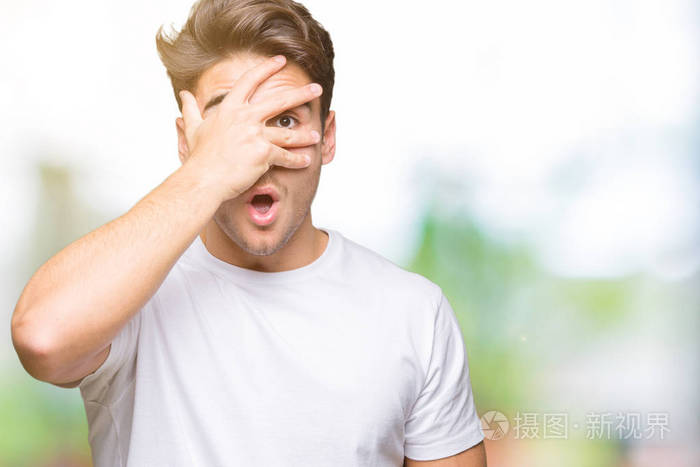 年轻的帅哥穿着白色t恤,在孤立的背景上偷看,震惊地